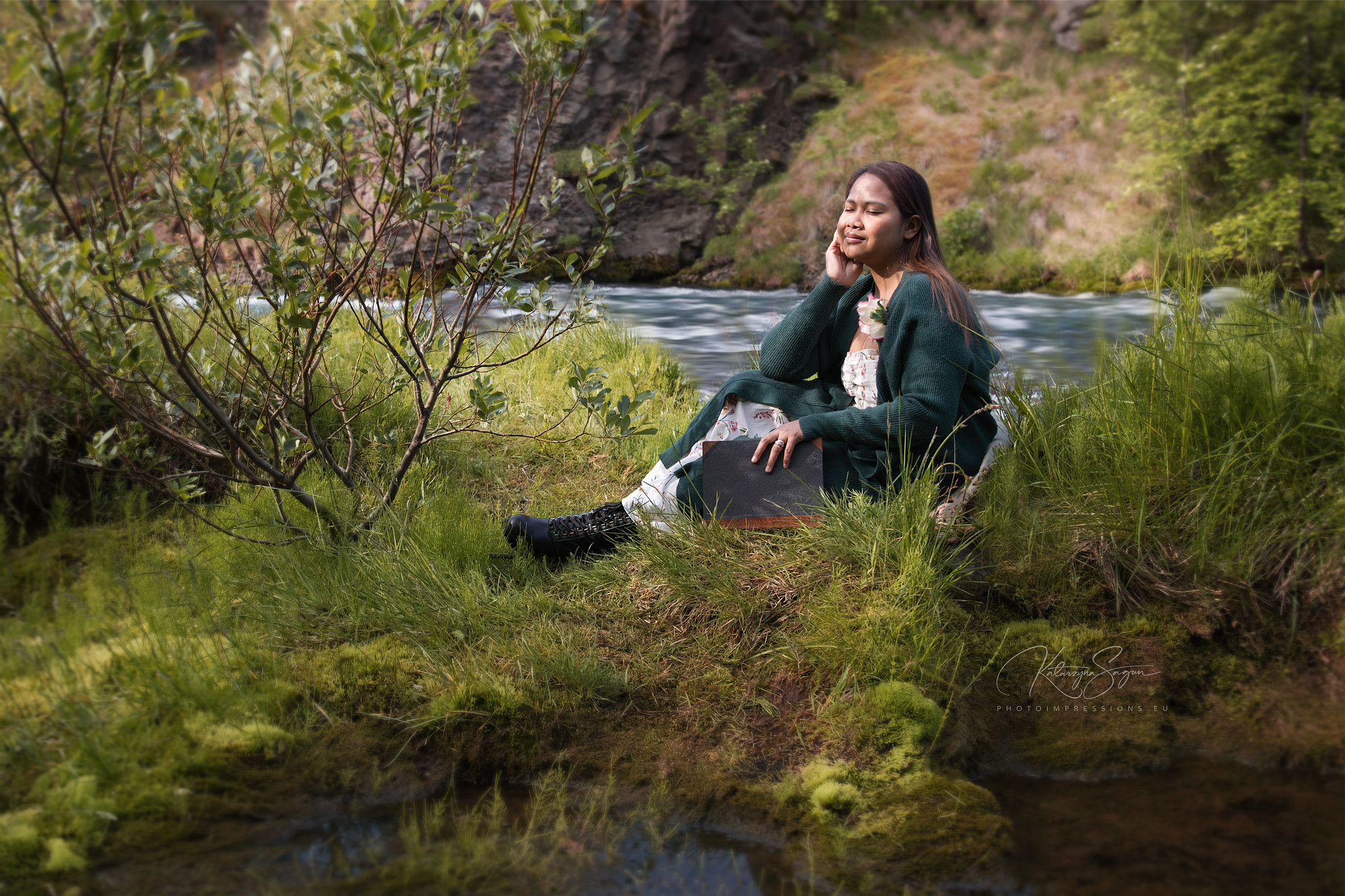 Woman in a green sweater and jeans sitting outdoors on a mossy hill in Iceland.