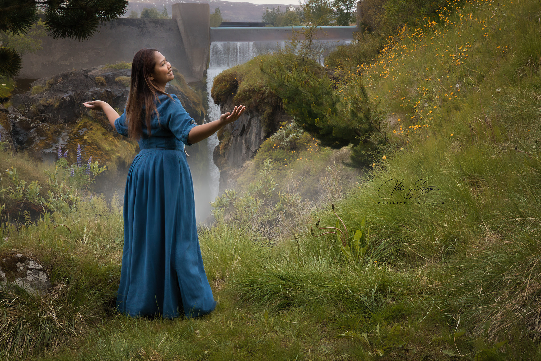 Full-body shot of a woman in a blue dress dancing by a faterfall in Iceland in Iceland.