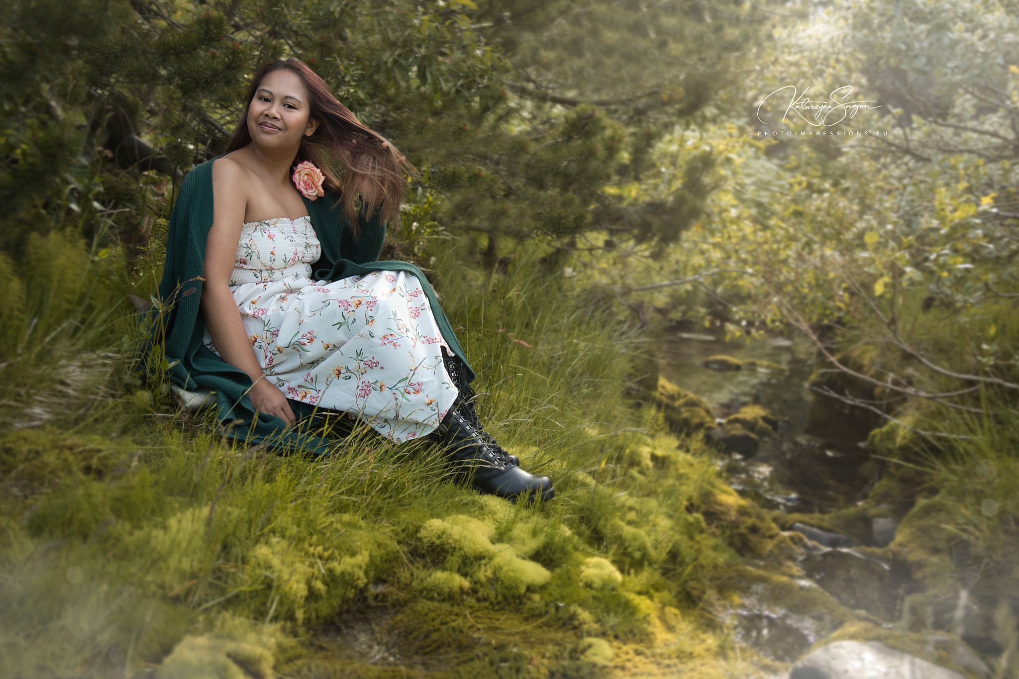 Woman in a white dress sitting on a green mossy bank during an Icelandic photoshoot.
