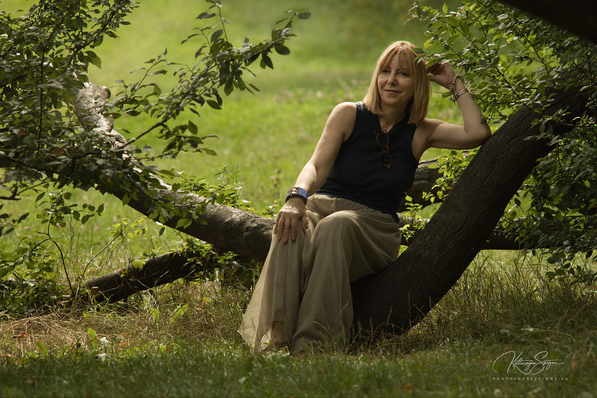 Solo outdoor portrait of a mature woman sitting on a large tree branch in an Icelandic garden.